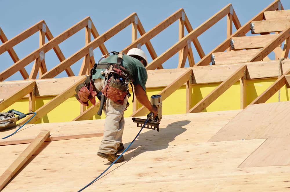 Construction worker drilling on top of the wooden roof