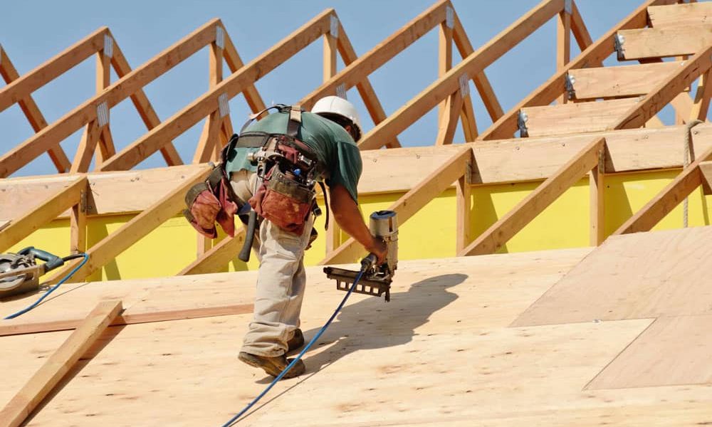 Construction worker drilling on top of the wooden roof