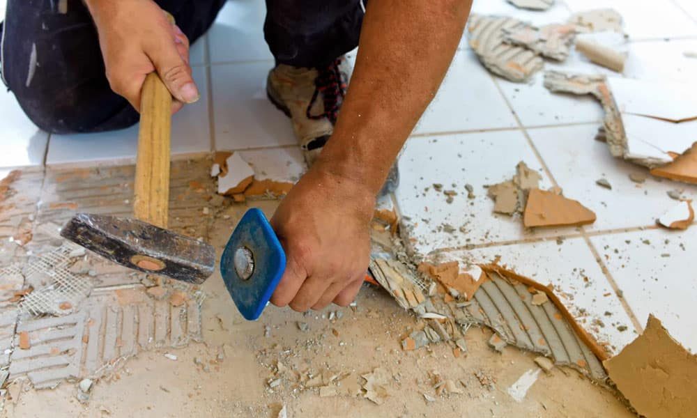 Man hammering the white bathroom tiles