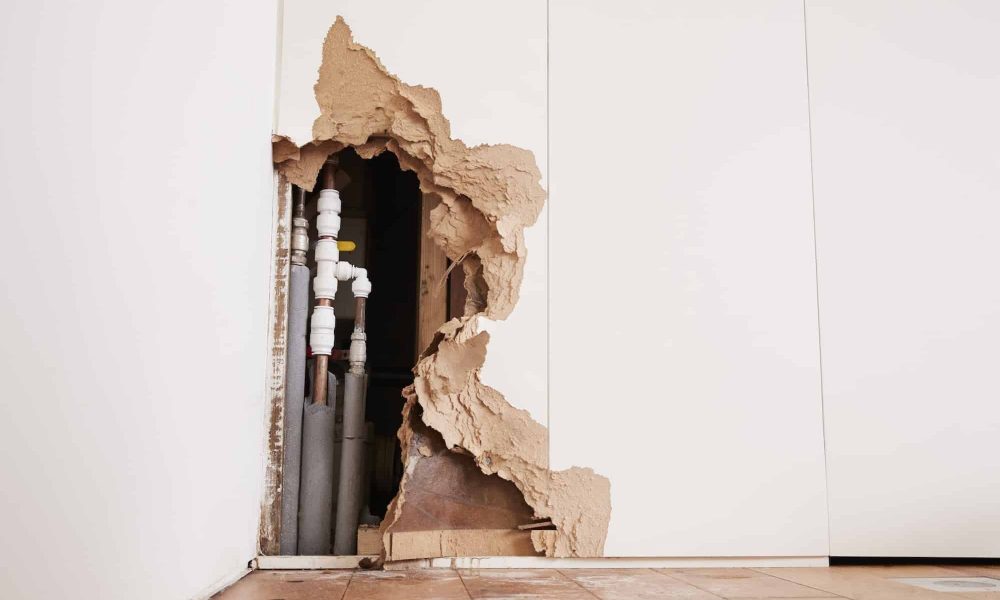 Damaged wall exposing burst water pipes